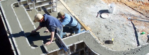 Two workers laying out inground pool steps using concrete forms.