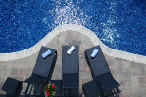 Three poolside deck chairs sit on a stone patio by the side of a clear, beautiful azure pool.