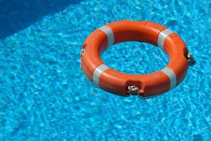 An orange life saver floats in a crystal-clear pool, part of the swimming pool’s safety equipment.