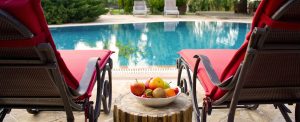 View of a backyard pool between two pool chairs and a side table filled with refreshments