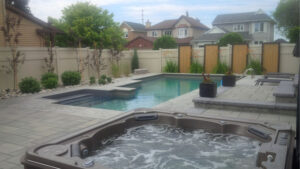 A backyard with a pool and a spa. Also is furnished, with houses in the background