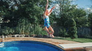 A young lady jumping off a diving board into a in-ground pool
