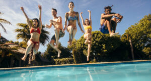 Image contains people jumping into a pool to start a pool party
